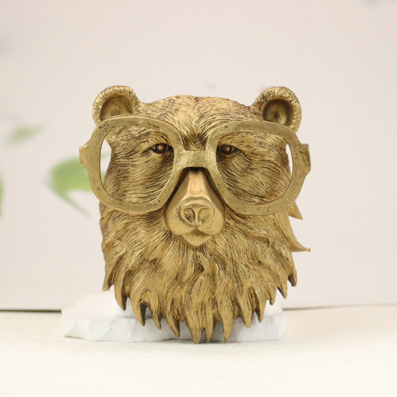 Gold bear head wall sculpture with oversized round glasses and textured fur details, mounted on white base with botanical blurred background | Modern faux taxidermy decor for contemporary interiors