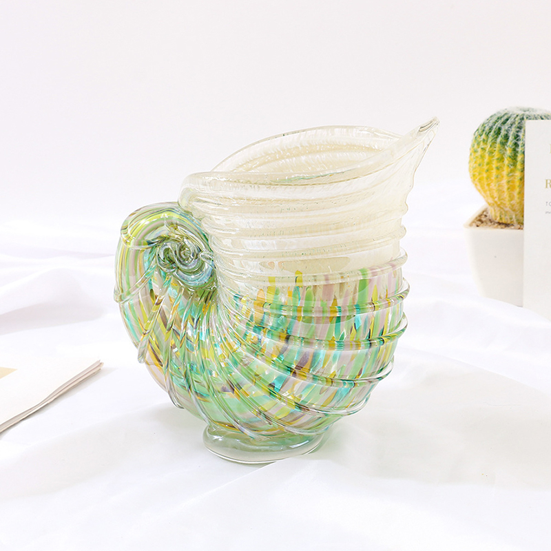 Coastal Chic nautilus shell glass vase with rainbow-colored stripes and spiral handle, staged with white potted succulent on light fabric backdrop under natural lighting.