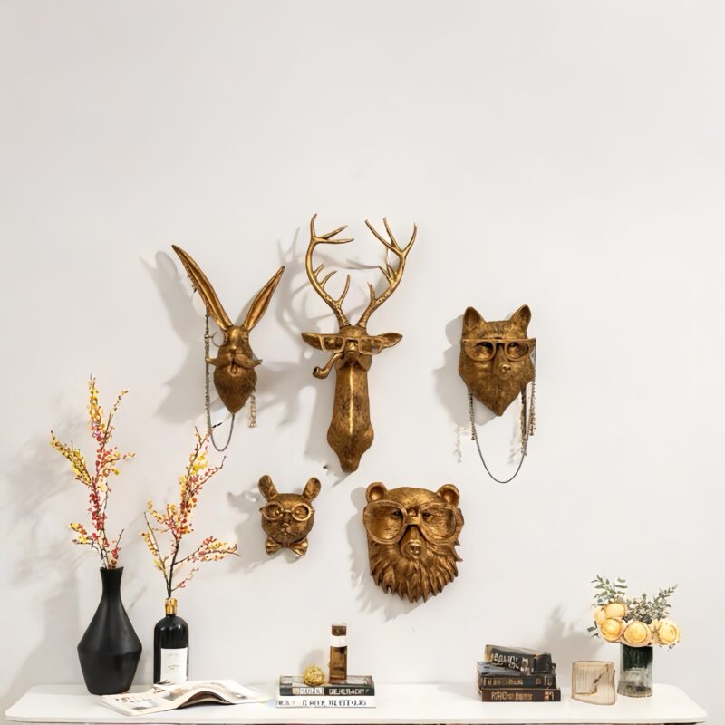 Gold animal head wall decor set (rabbit/deer/fox/mouse/bear) with eccentric eyewear, mounted on white wall above styled shelf: black vase with dried florals, red wine, perfume bottle, and art books including magazine