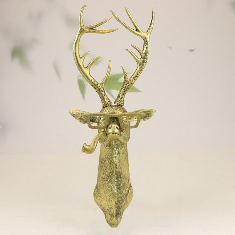Gold deer head wall sculpture with speckled antlers, square glasses & pipe on muted green leafy background | Whimsical faux taxidermy art for eclectic interiors