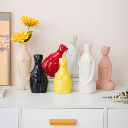Six ceramic female body vases in multicolor on white cabinet, yellow sunflowers in beige vase with ELC text decor