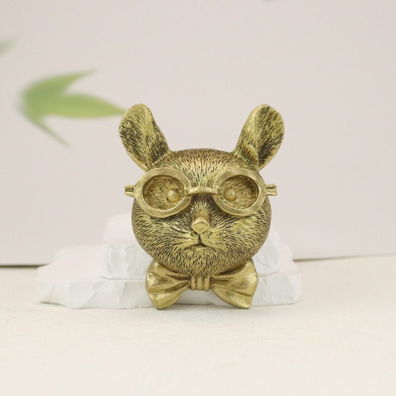Gold mouse head wall decor with round glasses & bow tie, textured fur details on white stone base with blurred green foliage background | Whimsical rodent wall art for modern interiors