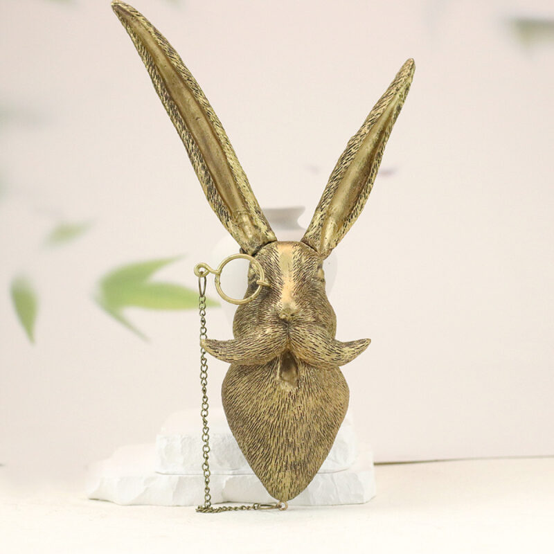 Gold rabbit head wall decor with monocle chain, textured fur details and elongated ears on white base, botanical blurred background | Vintage-inspired faux taxidermy wall art