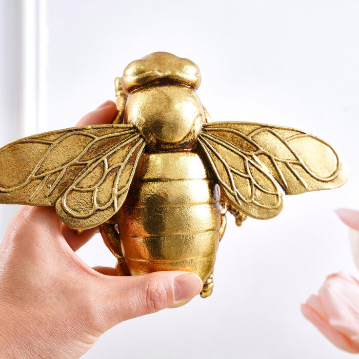 Handheld golden resin 3D bee wall sculpture with metallic luster, detailed wing veins, and layered abdomen on pure white background