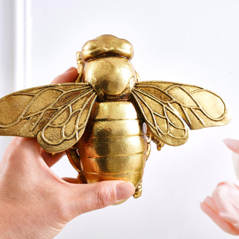 Handheld golden resin 3D bee wall sculpture with metallic luster, detailed wing veins, and layered abdomen on pure white background